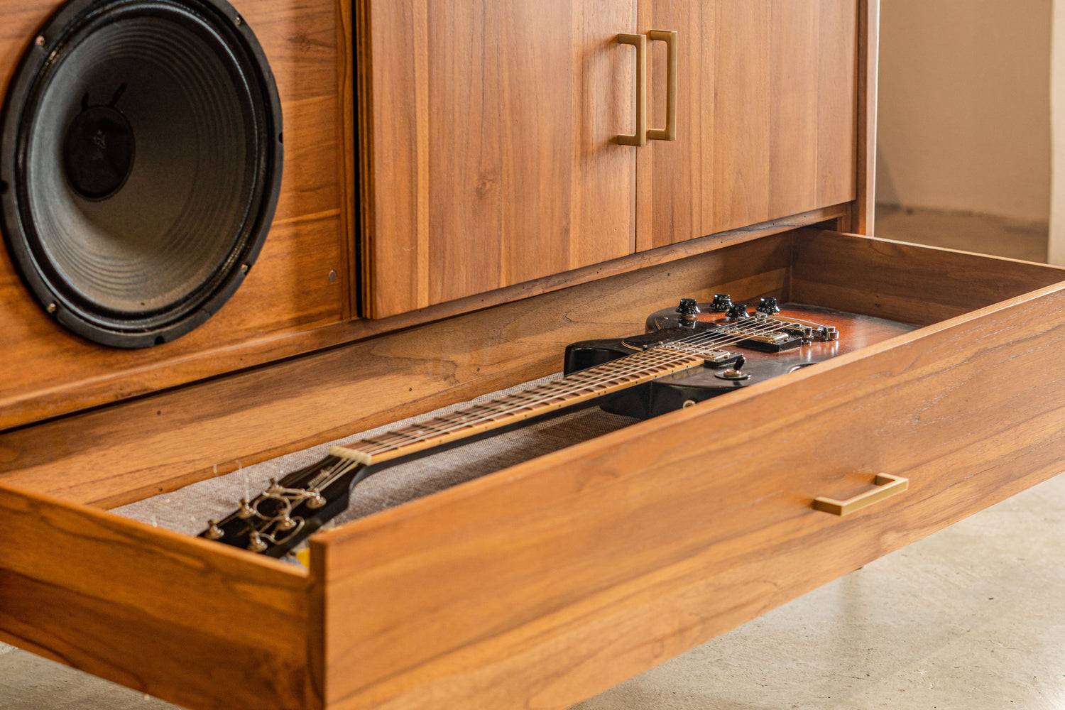 Wooden speaker cabinet drawer with a guitar inside.
